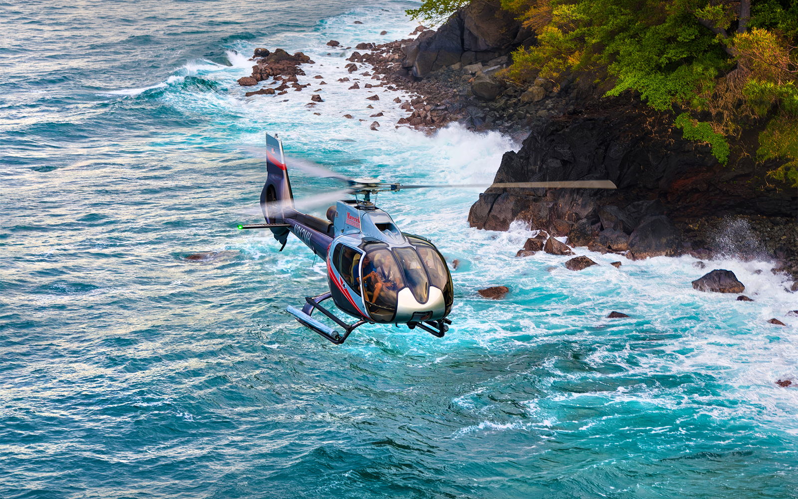 Helicopter flying over ocean near rocky coastline, Hana Rainforest, Hawaii.