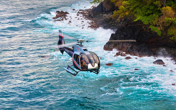 Helicopter flying over ocean near rocky coastline, Hana Rainforest, Hawaii.