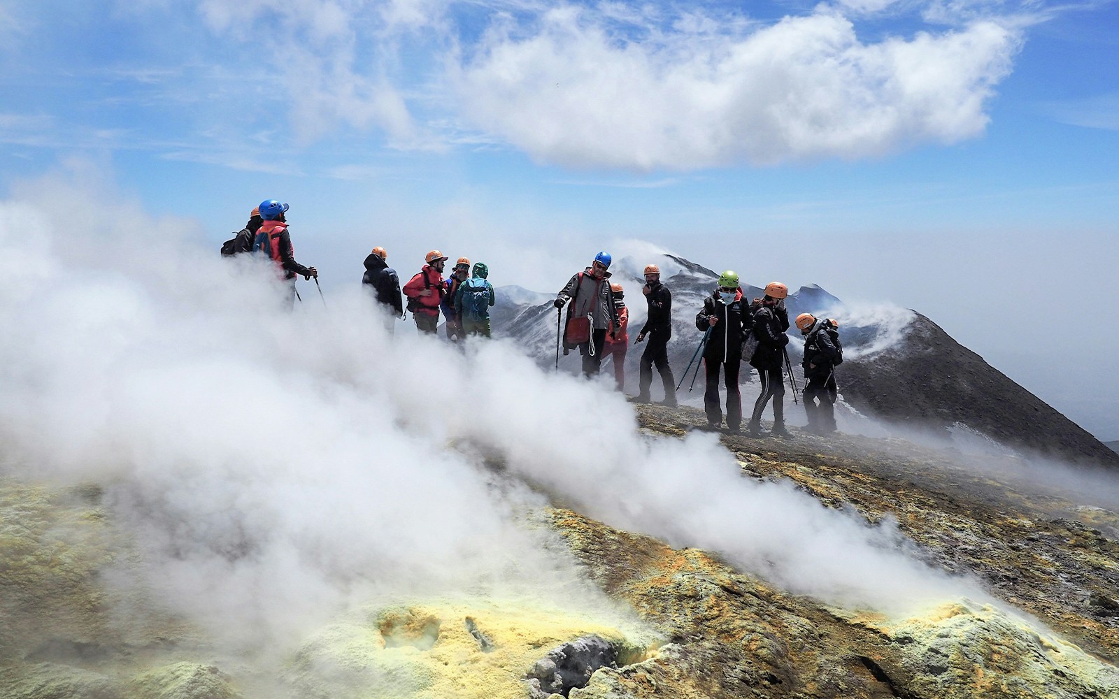 Hikers exploring the summit of Mount Etna with volcanic steam vents.