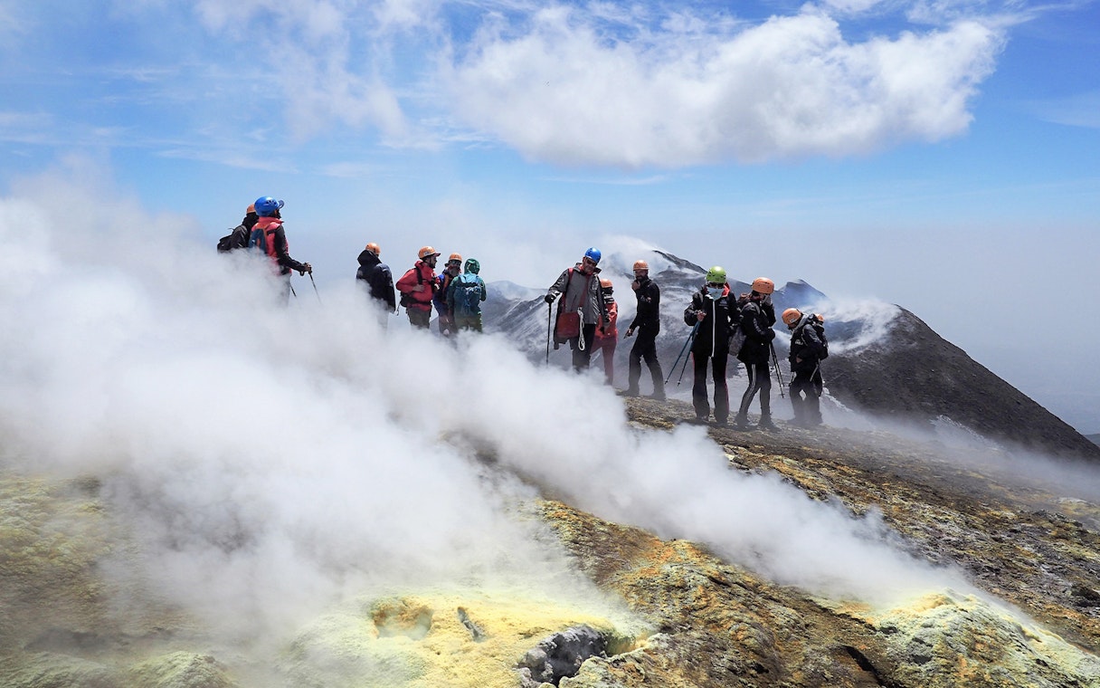 Hikers exploring the summit of Mount Etna with volcanic steam vents.