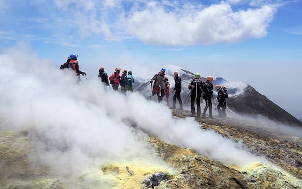 Hikers exploring the summit of Mount Etna with volcanic steam vents.