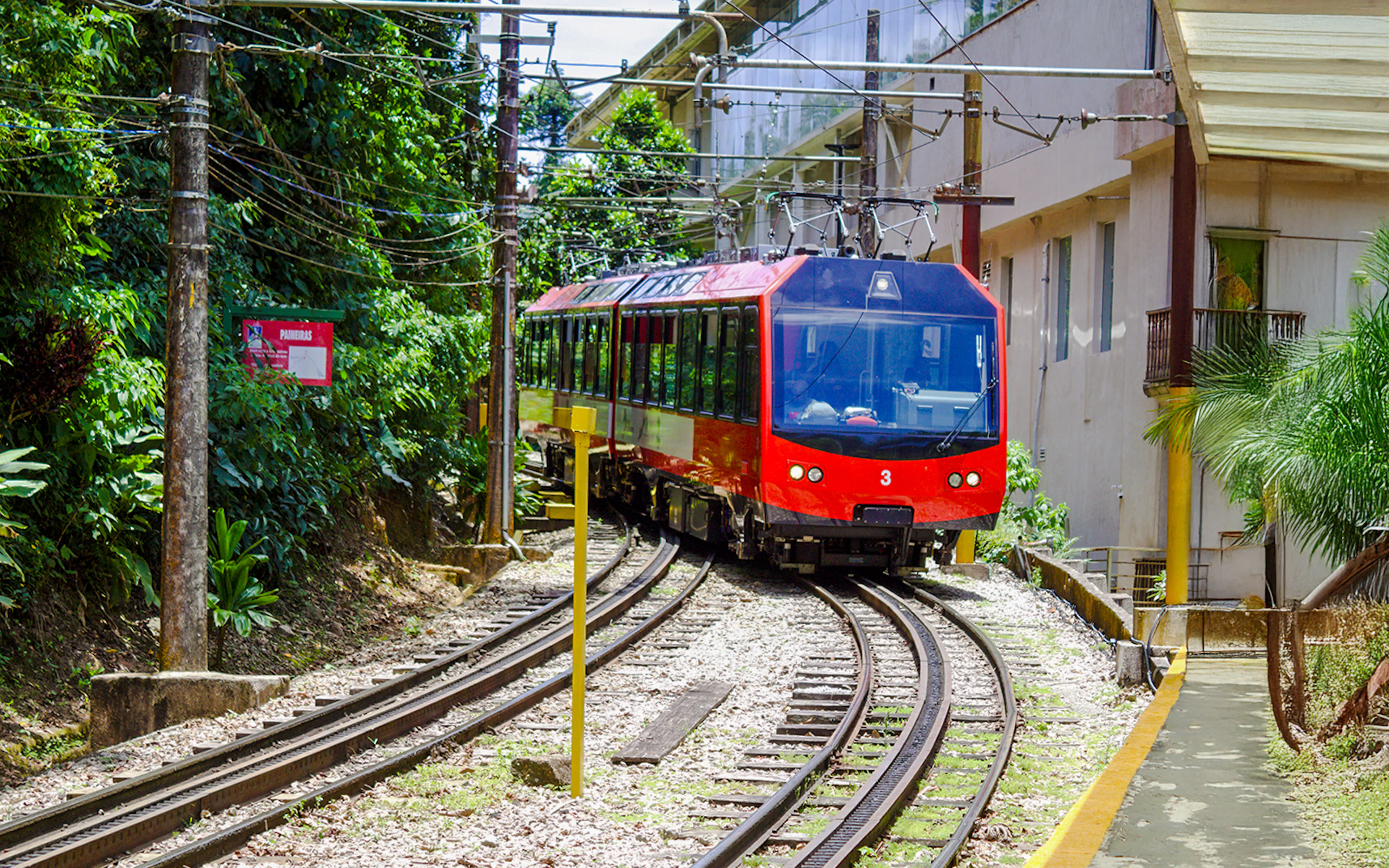 Red train on tracks surrounded by greenery, heading to Christ the Redeemer in Rio de Janeiro.