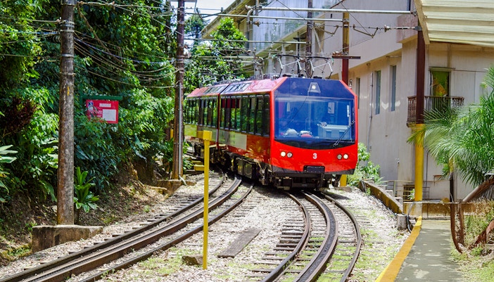 Red train on tracks surrounded by greenery, heading to Christ the Redeemer in Rio de Janeiro.