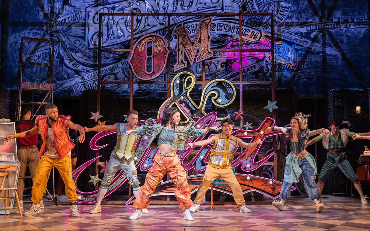 Performers dancing energetically on stage in the musical "& Juliet" with vibrant neon backdrop.