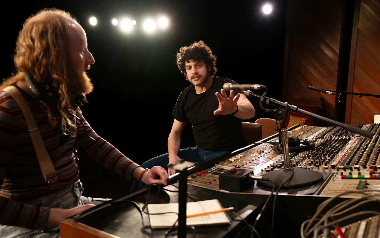 Recording studio session with two people discussing sound mixing at a control panel, related to stereophonic tours.