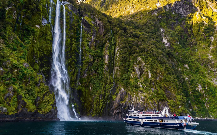 Cruise boat near waterfall in Milford Sound, New Zealand, on Te Anau day tour.