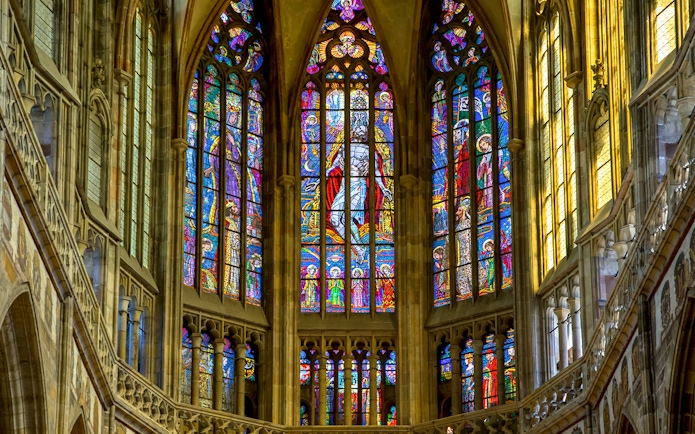 Stained glass windows inside St Vitus Cathedral, Prague, depicting religious scenes.