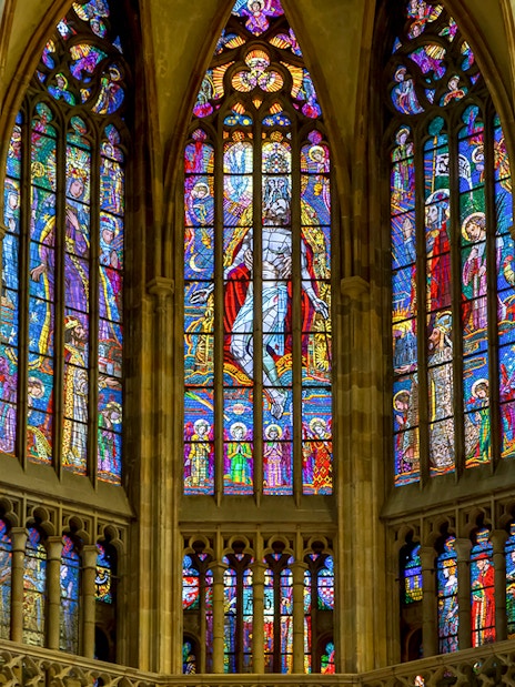 Stained glass windows inside St Vitus Cathedral, Prague, depicting religious scenes.