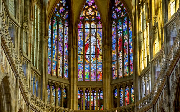Stained glass windows inside St Vitus Cathedral, Prague, depicting religious scenes.