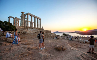 Temple of Poseidon at Cape Sounion during sunset with visitors exploring the site.