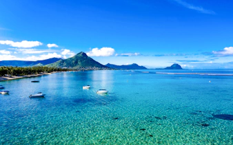 Flic en Flac beach with boats, palm trees, and Tourelle du Tamarin mountain, Mauritius.