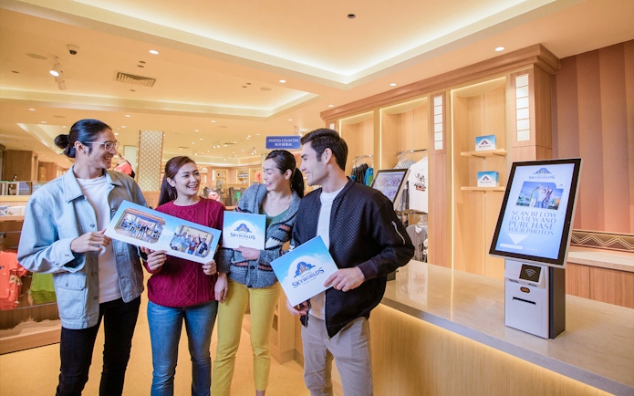 Visitors holding photos at Genting SkyWorlds theme park photo counter.