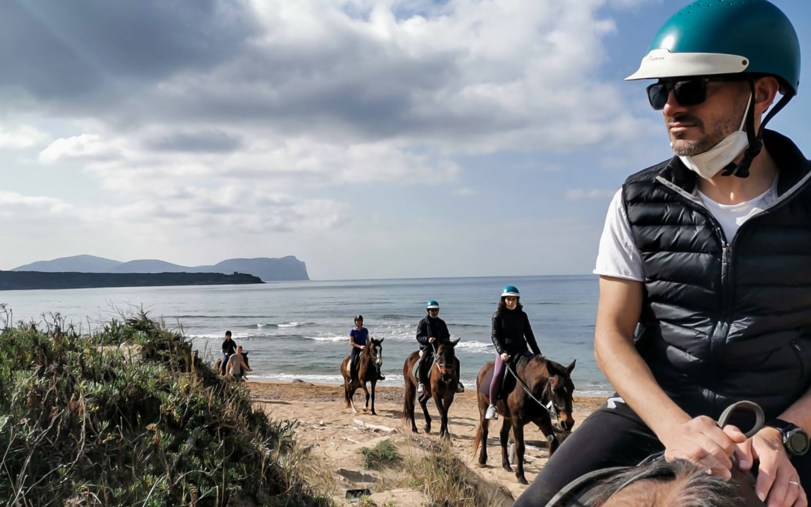 Horseback riders on Porto Ferro beach with Lake Baratz in the background.