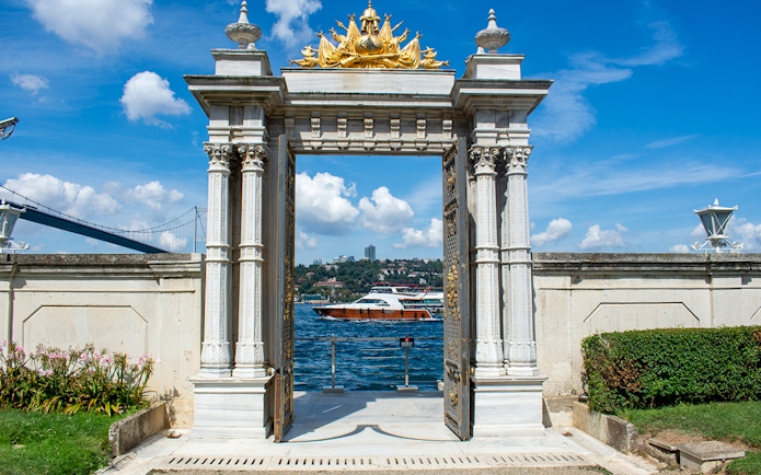 Main gate of Beylerbeyi Palace in Istanbul overlooking the Bosphorus with a boat passing by.