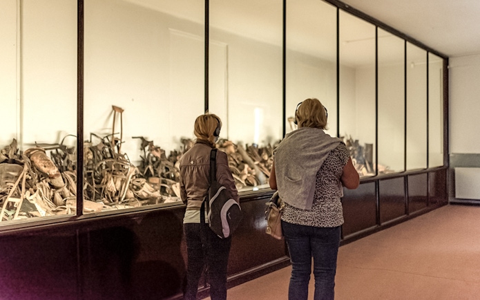 Visitors viewing personal artifacts at Auschwitz museum exhibit.