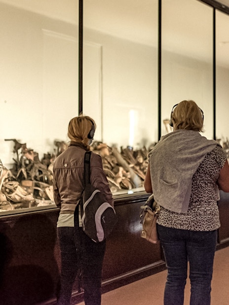 Visitors viewing personal artifacts at Auschwitz museum exhibit.