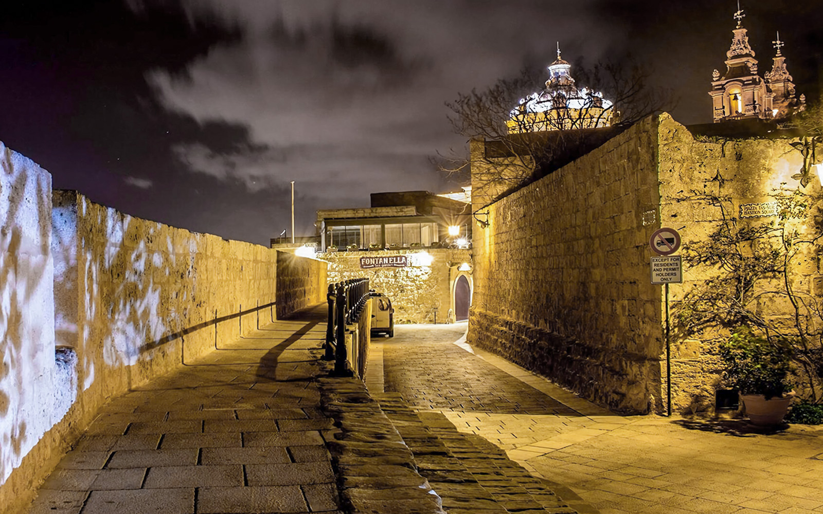 Historic stone pathway in Malta illuminated at night with church domes in the background.