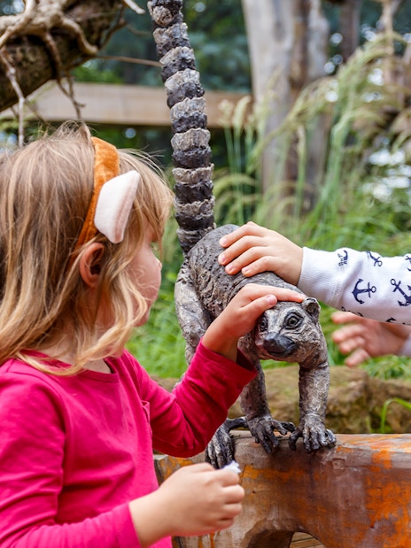 Children interacting with a lemur statue at a zoo.