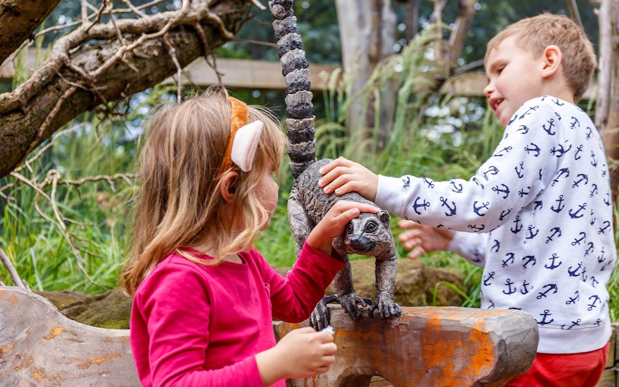 Children interacting with a lemur statue at a zoo.