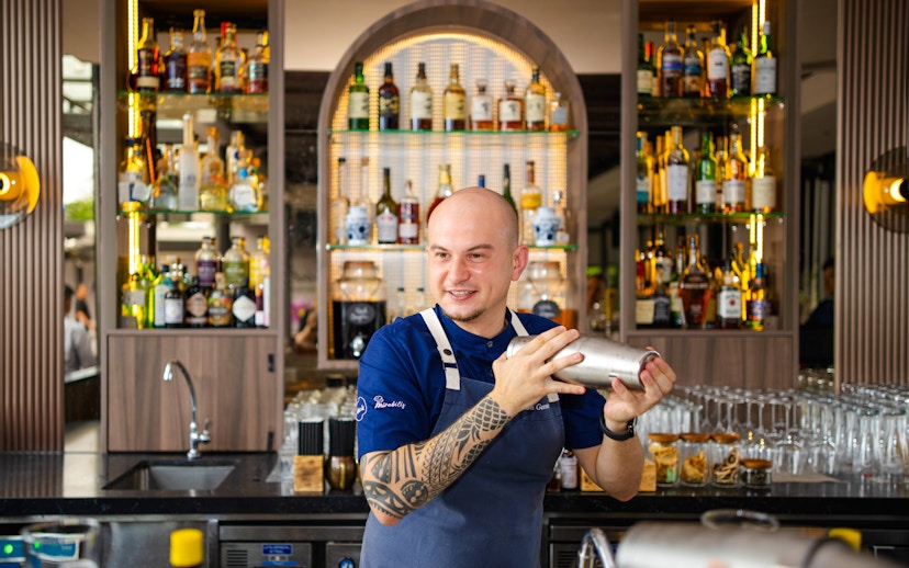 Bartender shaking cocktail at Mirabilis bar, Singapore cable car in background.