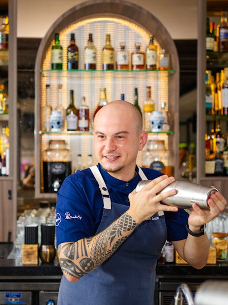 Bartender shaking cocktail at Mirabilis bar, Singapore cable car in background.