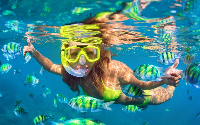 Woman snorkeling among colorful fish in clear tropical waters.