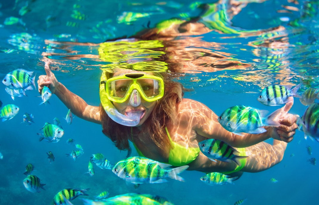 Woman snorkeling among colorful fish in clear tropical waters.