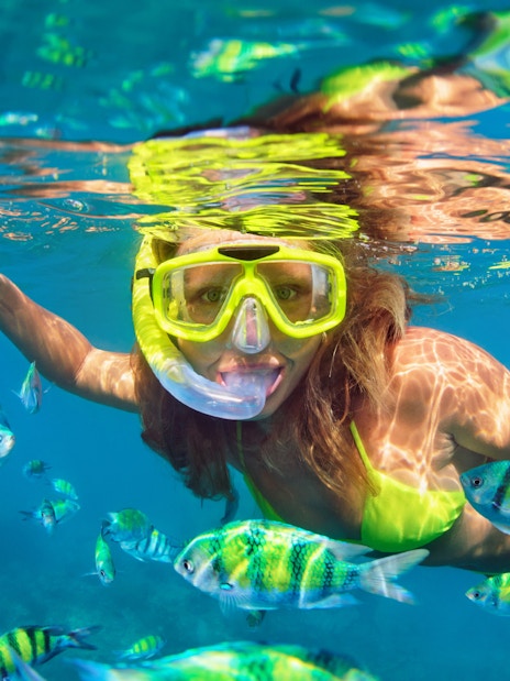 Woman snorkeling among colorful fish in clear tropical waters.