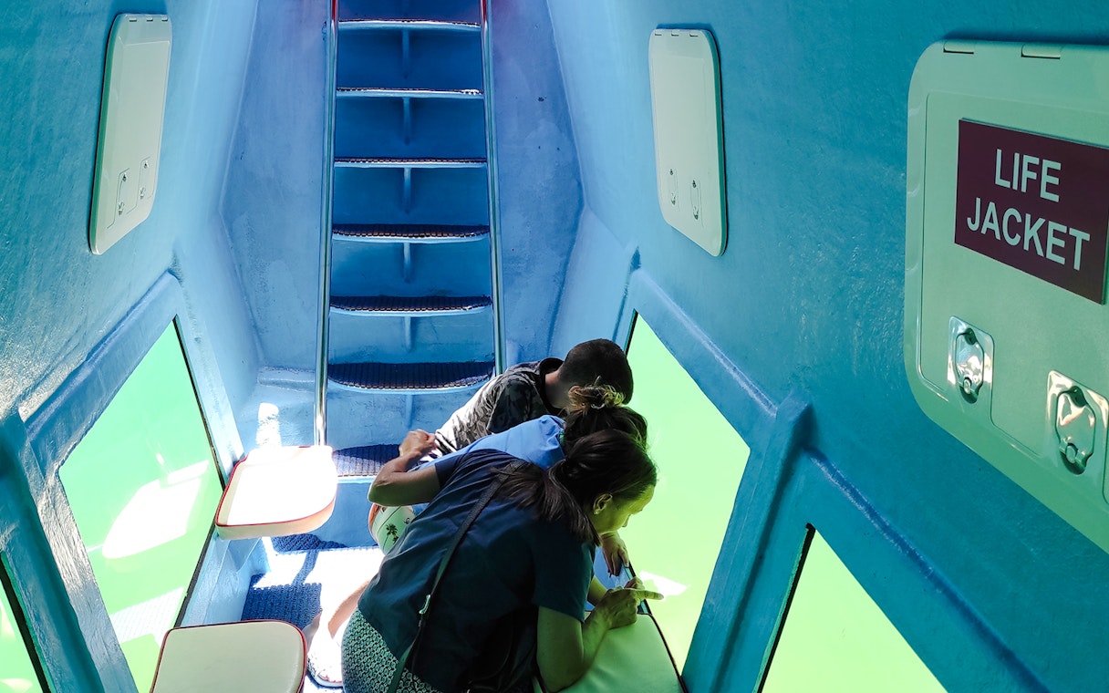 Underwater submarine interior with tourists viewing Boka Bay, Kotor through windows.