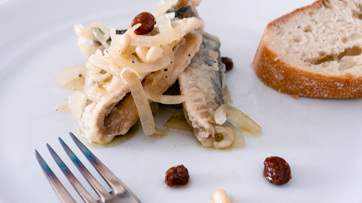 Venetian marinated sardines with onions and raisins on a white plate.