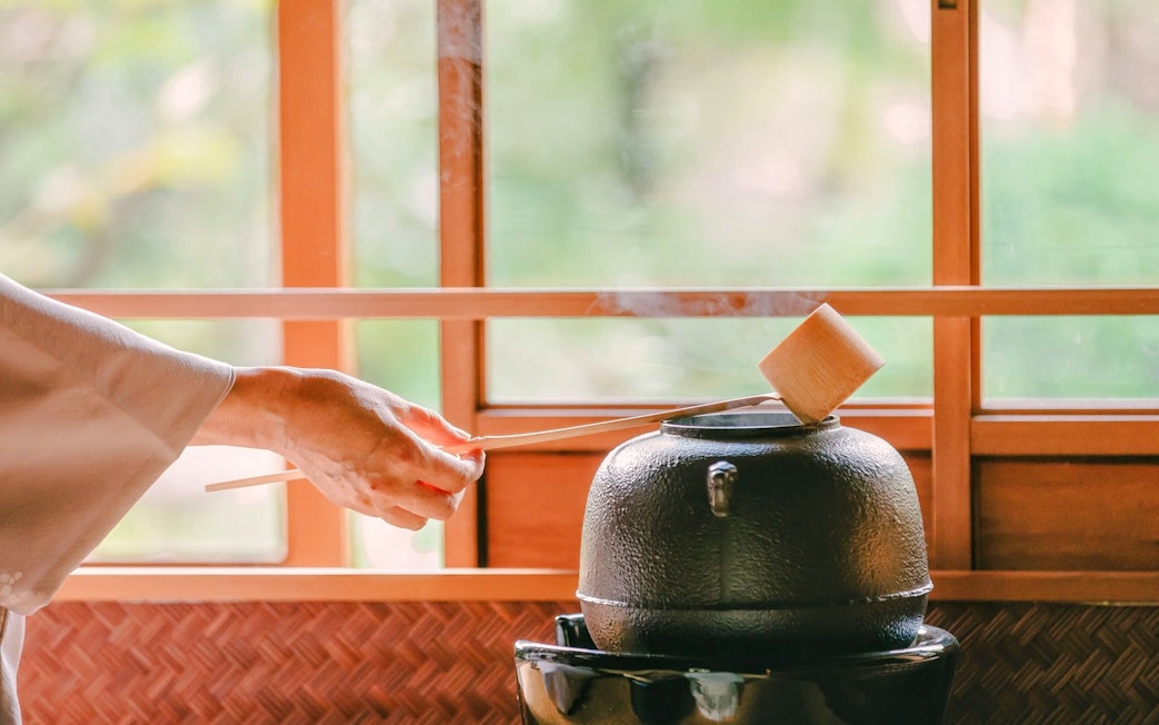 Hand pouring hot water into a teapot during a traditional tea ceremony in Japan.
