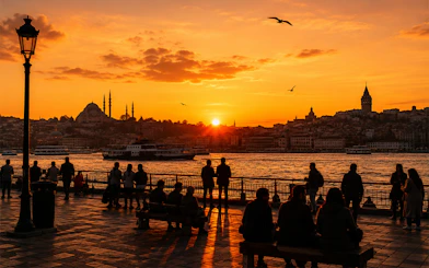 Galata Tower and Istanbul skyline at sunset with people by the waterfront.