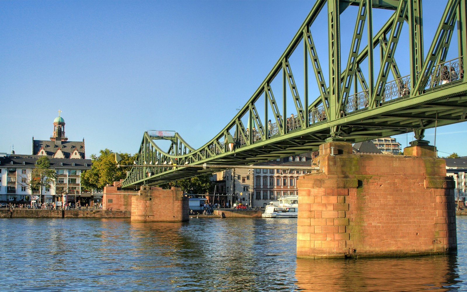 Eiserner Steg bridge over the Main River in Frankfurt, Germany, with city skyline in the background.