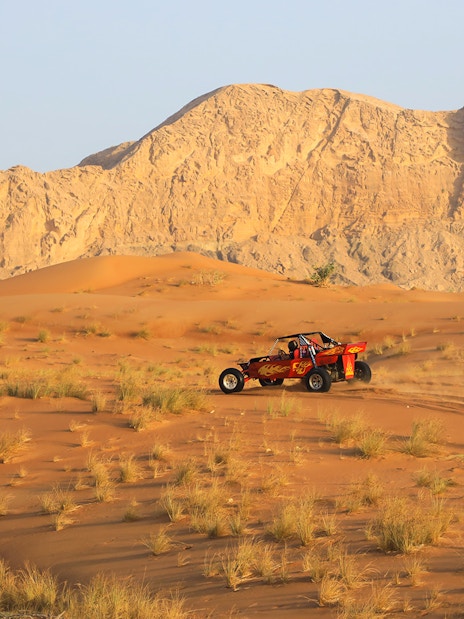 Dune buggy driving on Arabian desert dunes with rocky mountains in the background.