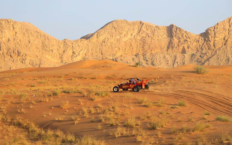 Dune buggy driving on Arabian desert dunes with rocky mountains in the background.