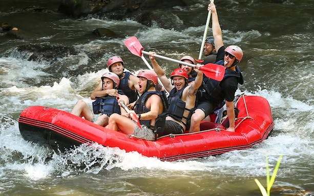 Group rafting on Ayung River in Ubud, navigating rapids in a red inflatable raft.