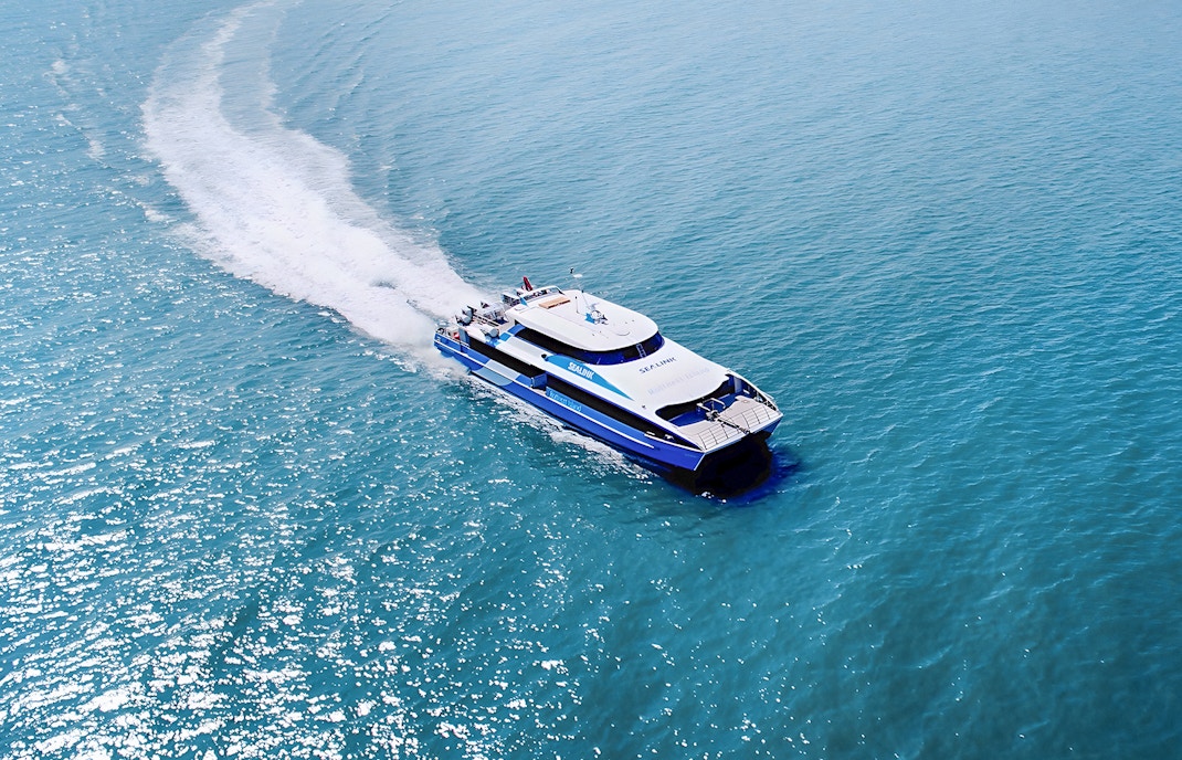 Eine Gruppe von Touristen genießt einen sonnigen Tag auf der Rottnest Island Guided Bus Tour, mit Blick auf den Ozean und die Fähre, die am Dock in Perth oder Fremantle auf die Rückkehr wartet.