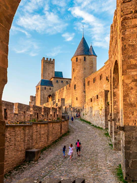 Medieval walls and towers of Carcassonne in Aude, Occitanie, with tourists walking along cobblestone path.