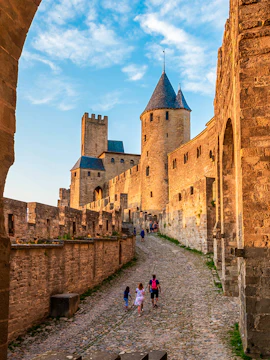 Medieval walls and towers of Carcassonne in Aude, Occitanie, with tourists walking along cobblestone path.