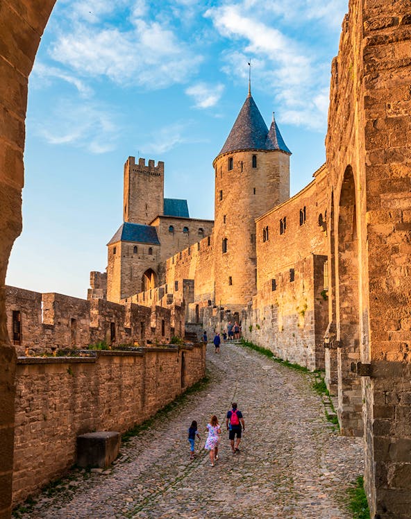 Medieval walls and towers of Carcassonne in Aude, Occitanie, with tourists walking along cobblestone path.