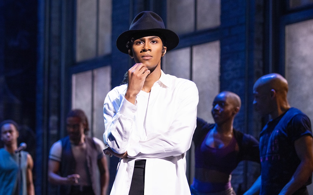 Performer in MJ The Musical on stage with dancers in the background.