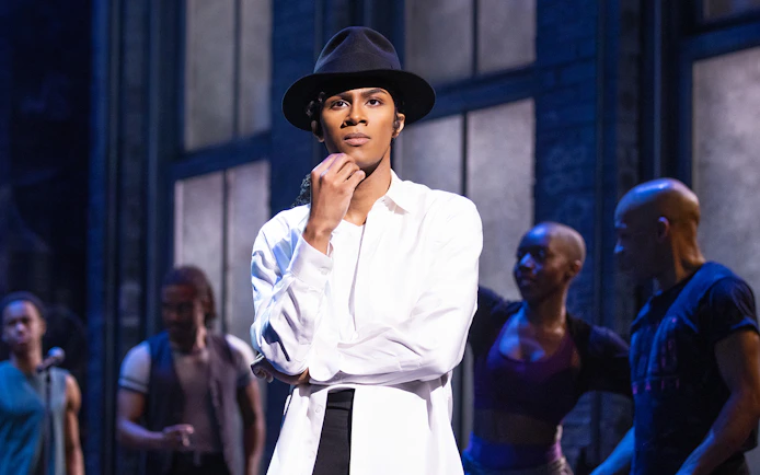 Performer in MJ The Musical on stage with dancers in the background.