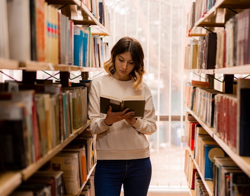 Person reading a book in a library aisle.