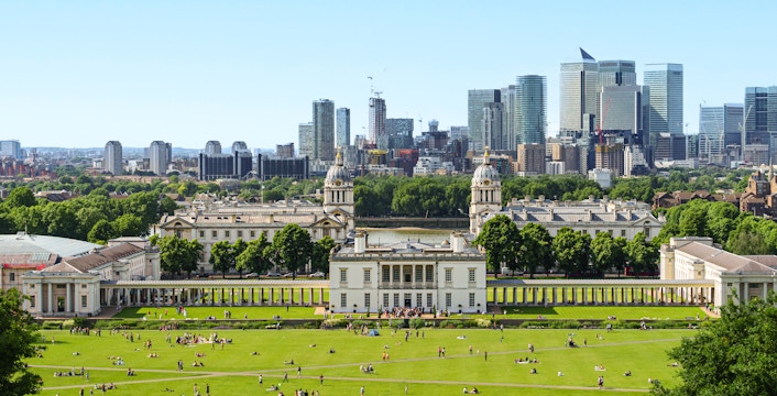 Panoramic view of Canary Wharf skyline from Greenwich Park, London, with historic buildings in foreground.