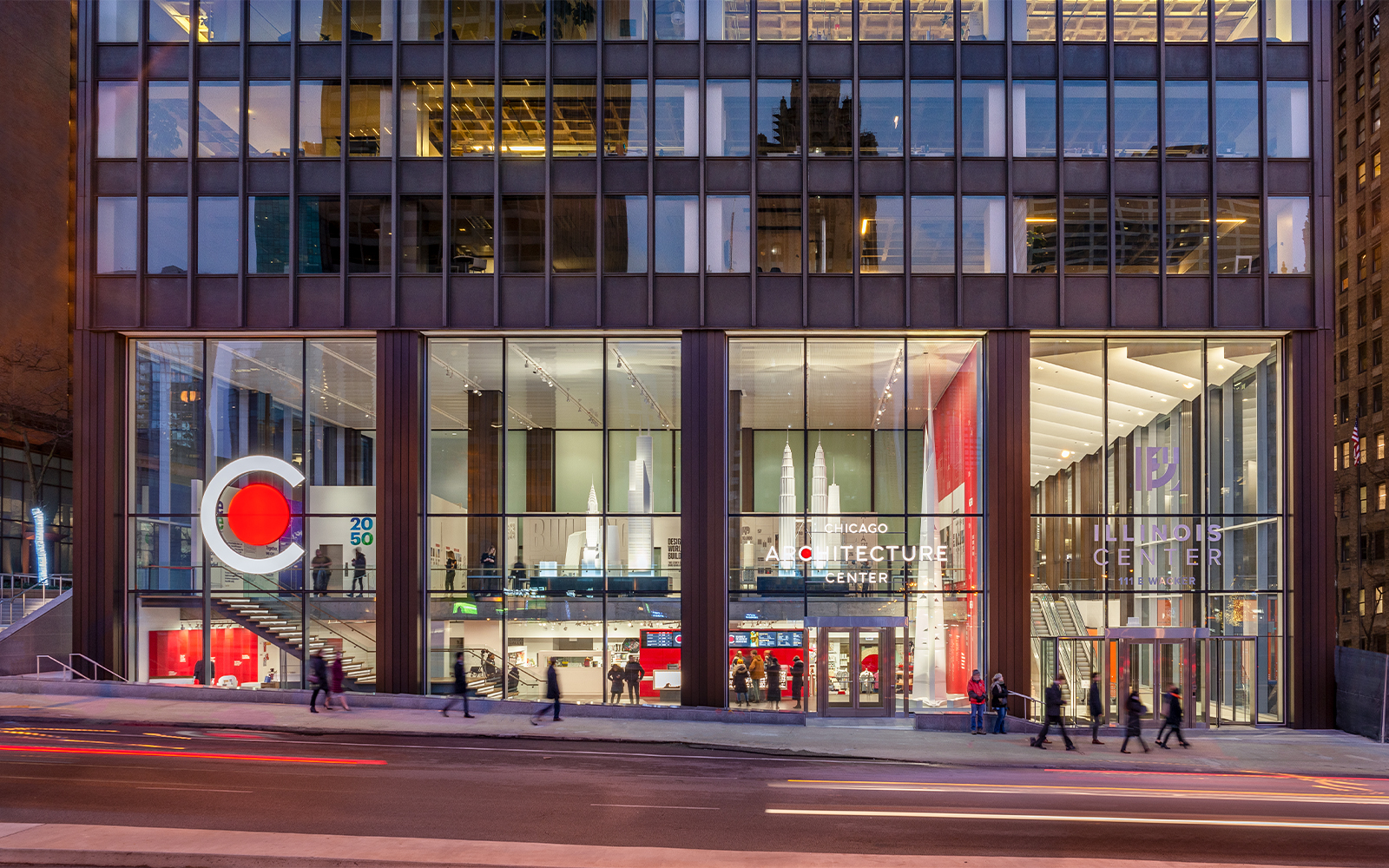 Chicago Architecture Center facade illuminated at night with people walking by.