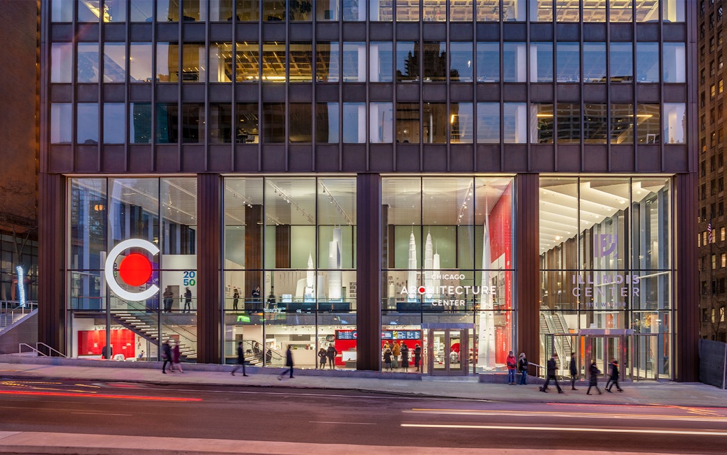 Chicago Architecture Center facade illuminated at night with people walking by.