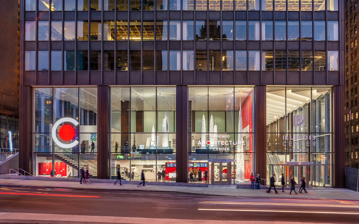 Chicago Architecture Center facade illuminated at night with people walking by.