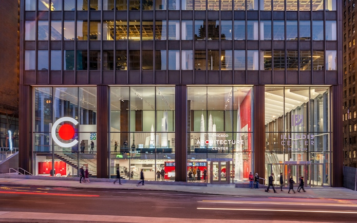 Chicago Architecture Center facade illuminated at night with people walking by.
