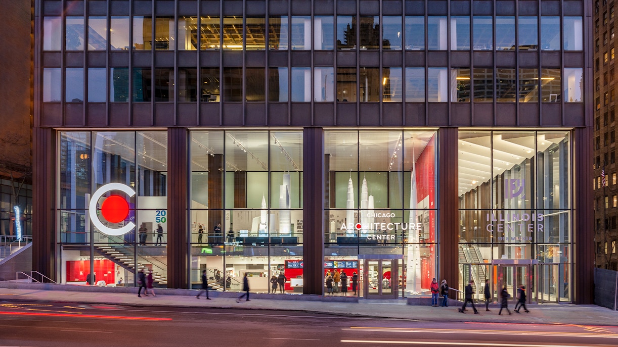 Chicago Architecture Center facade illuminated at night with people walking by.
