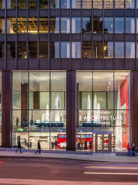 Chicago Architecture Center facade illuminated at night with people walking by.